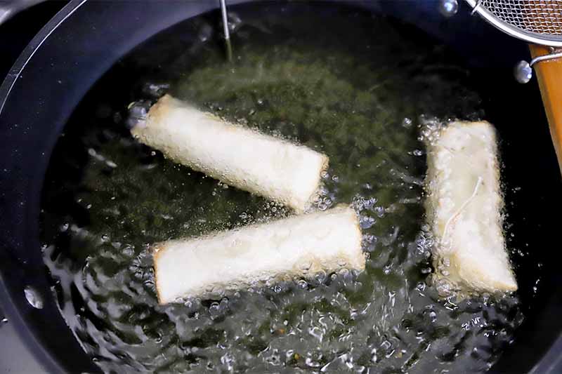 Horizontal image of frying filled wonton wrappers in hot and bubbling oil in a pot.