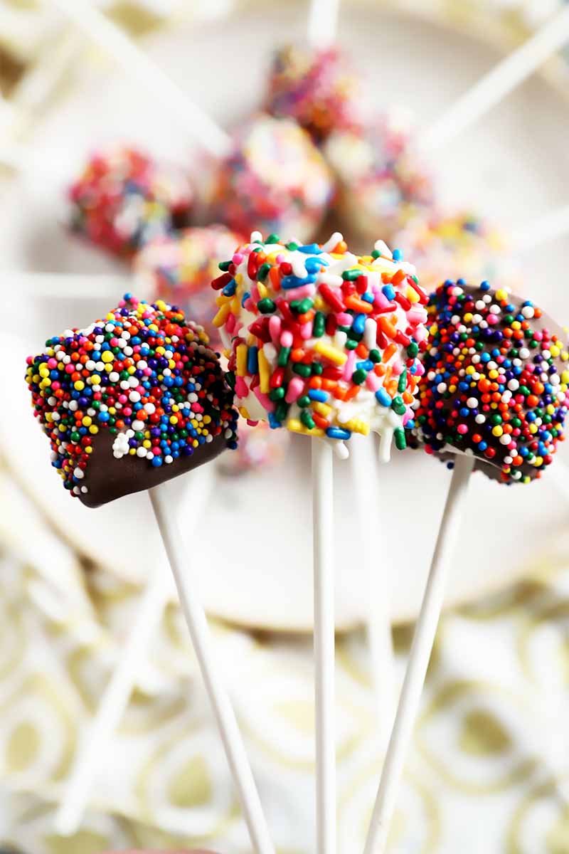 Vertical image of marshmallow pops covered in assorted colorful sprinkles.