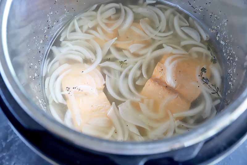 Horizontal image of cooked pieces of fish fillet poaching in a pot with slices onions and liquids.