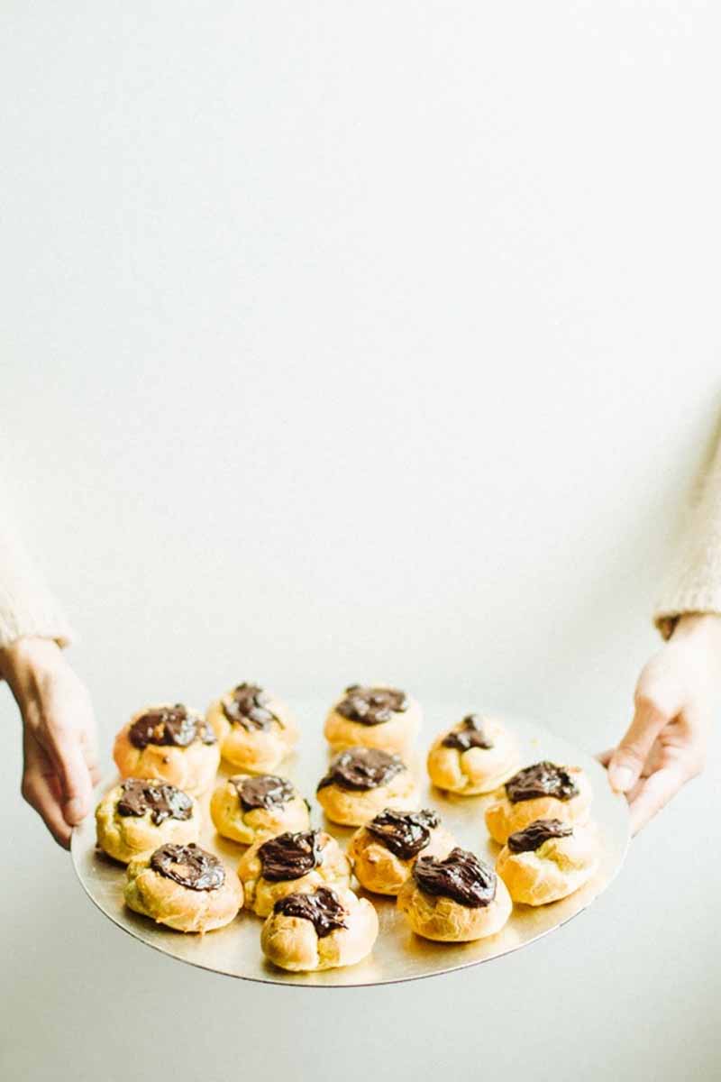 Vertical image of hands holding a serving platter with small, round pastries topped with a cocoa glaze.