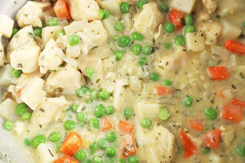 Horizontal image of a thick and creamy savory mixture of peas, carrots, potatoes, and white meat.