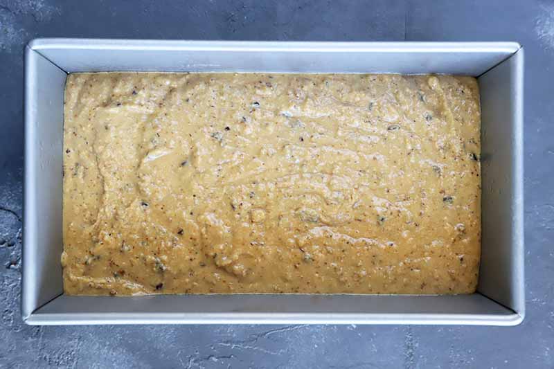 Horizontal image of a light yellow batter in a metal loaf pan.