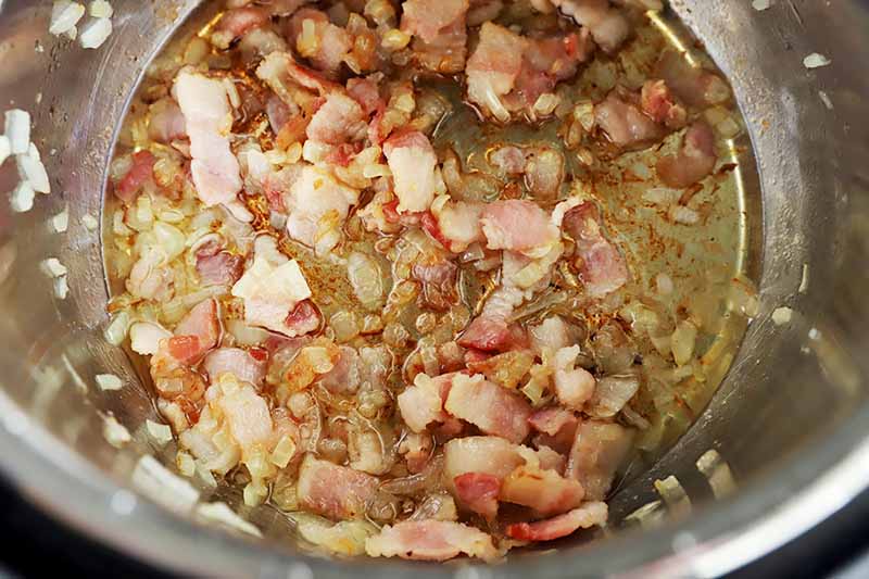 Horizontal image of cooking bacon and onions in a pot.