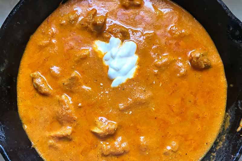 Horizontal image of a skillet with stew and a dollop of yogurt.