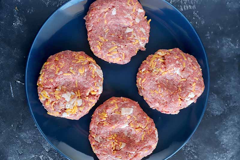 Horizontal image of patties made of raw ground meat on a dark navy plate.