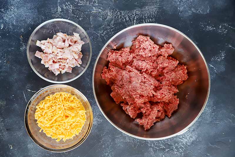 Horizontal image of a bowl of raw ground meat, raw pork belly pieces, and shredded cheddar.