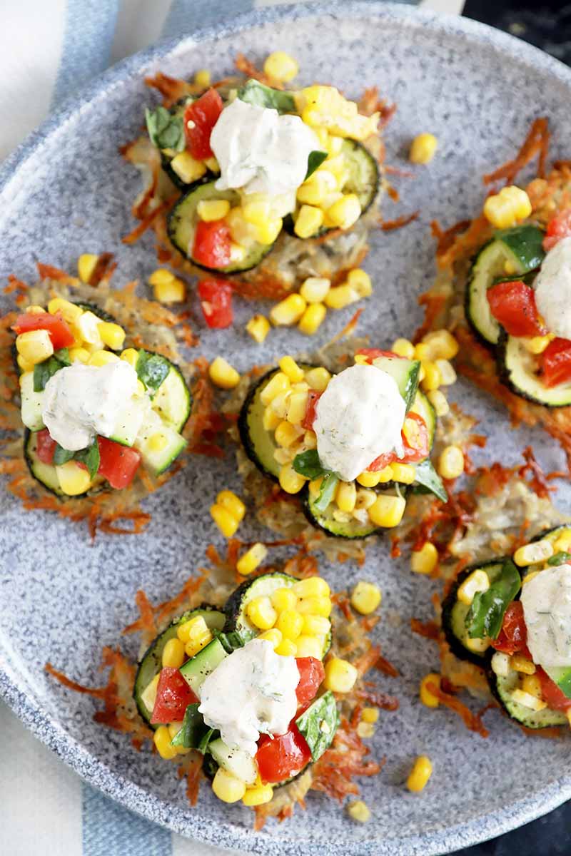 Vertical top-down image of individual servings of savory pancakes topped with slices of vegetables, a chunky salsa, and dollops of yogurt.