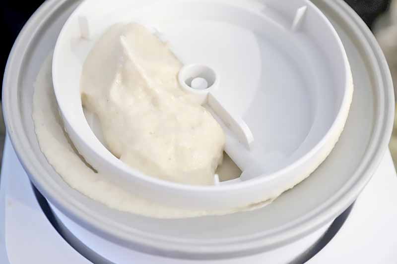 Horizontal image of an ice cream maker with a thick light orange mixture.