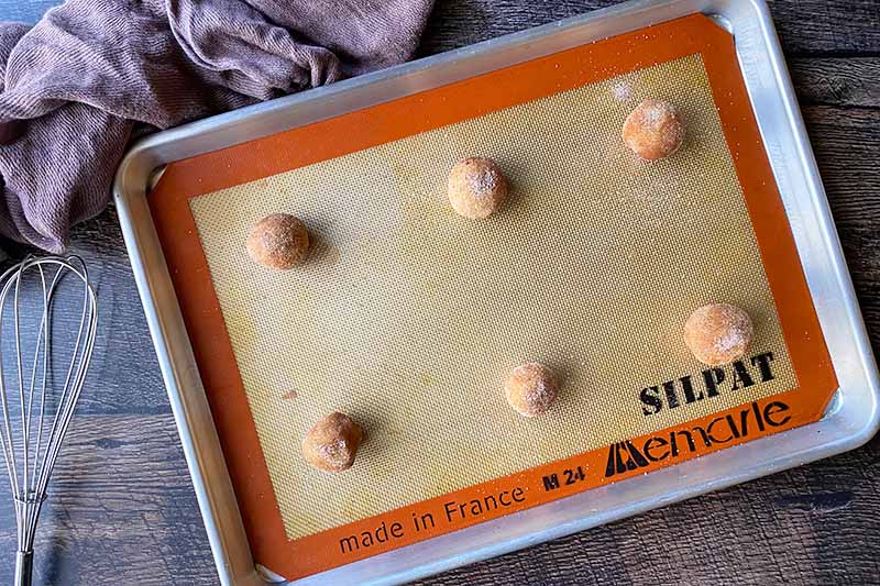 Horizontal image of 6 mounds of unbaked dough on a tray lined with a silicone mat.