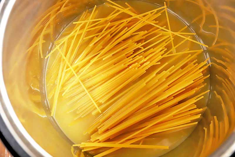 Horizontal image of raw noodles broken in half in a pot of water.