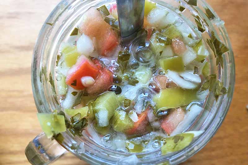 Horizontal image of mixing a mixture of chopped vegetables and liquids in a glass jar.