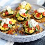 Horizontal image of a round gray plate with individual savory potato pancakes topped with assorted vegetables and yogurt.