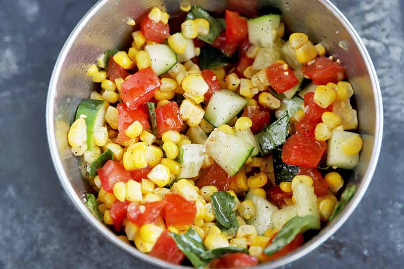 Horizontal image of a bowl filled with a mixed salad of cucumber, tomato, and corn.