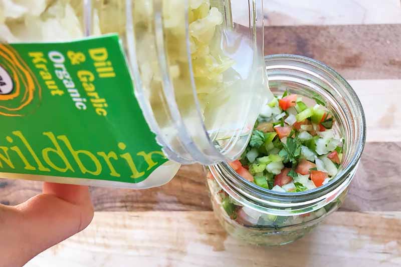 Horizontal image of pouring brine into a jar with chopped vegetables.