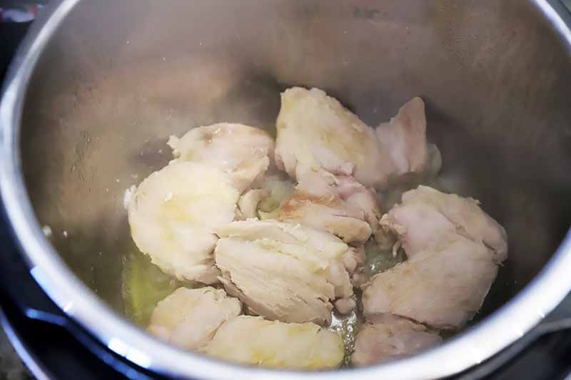 Horizontal image of cooking poultry pieces in a pot.
