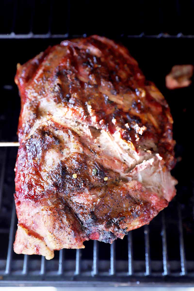 Vertical image of a large piece of meat cooking on the grill.