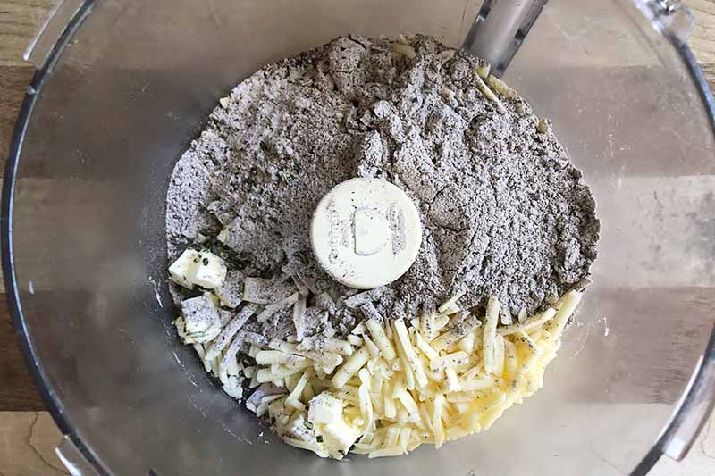 Horizontal image of flour, butter, and shredded cheese in a food processor.