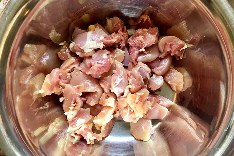 Horizontal image of raw poultry pieces in a metal bowl.