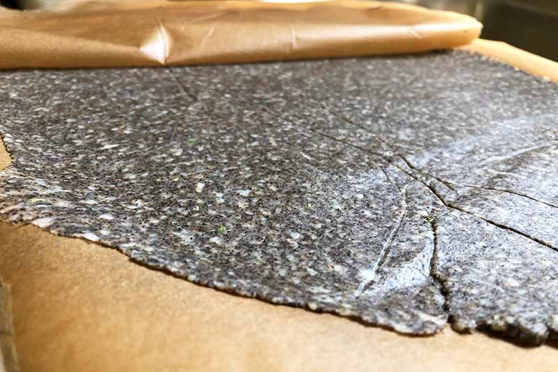 Horizontal image of a thin layer of dark brown dough between two sheets of parchment paper.