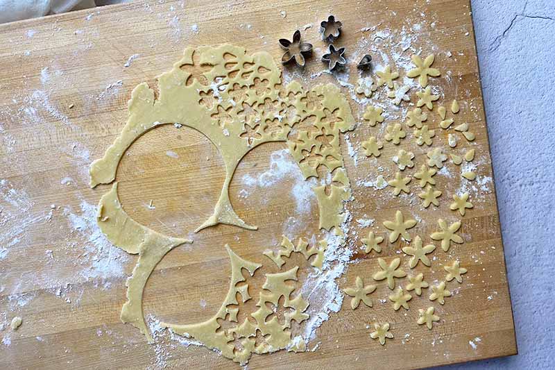 Horizontal image of cutting out mini shapes of flowers in a flat pastry dough.