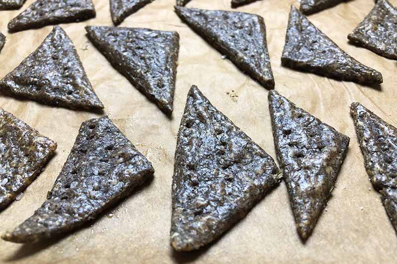 Horizontal image of dark brown triangular crackers on a lined baking sheet.