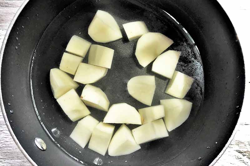 Horizontal image of a pot of water and chopped potatoes.