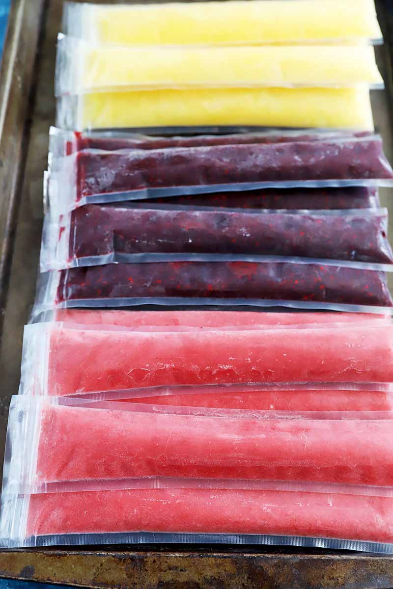 Vertical image of pink, purple, and yellow popsicles on a tray