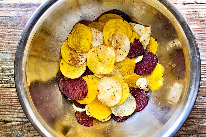 Horizontal image of seasoned thinly sliced beets and parsnips in a metal bowl.