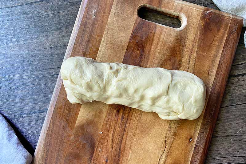Horizontal image of a log of dough on a wooden cutting board.