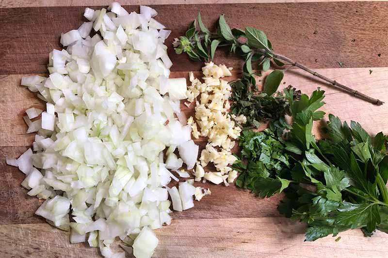 Horizontal image of a pile of chopped onions, garlic, and herbs.