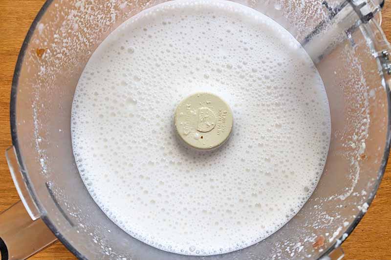 Horizontal image of a frothy creamy liquid in a food processor.