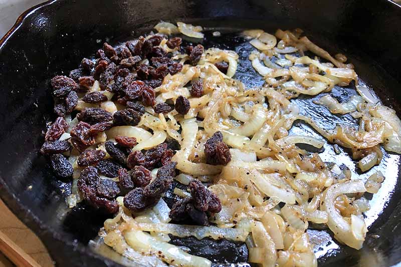 Horizontal image of caramelized onions and raisins in a cast iron pan.