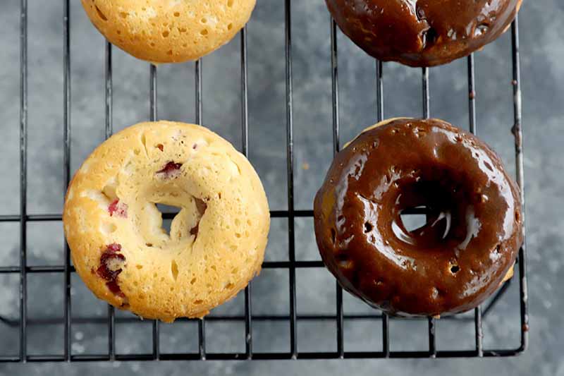 Horizontal image of unglazed and glazed baked doughnuts on a cooling rack.