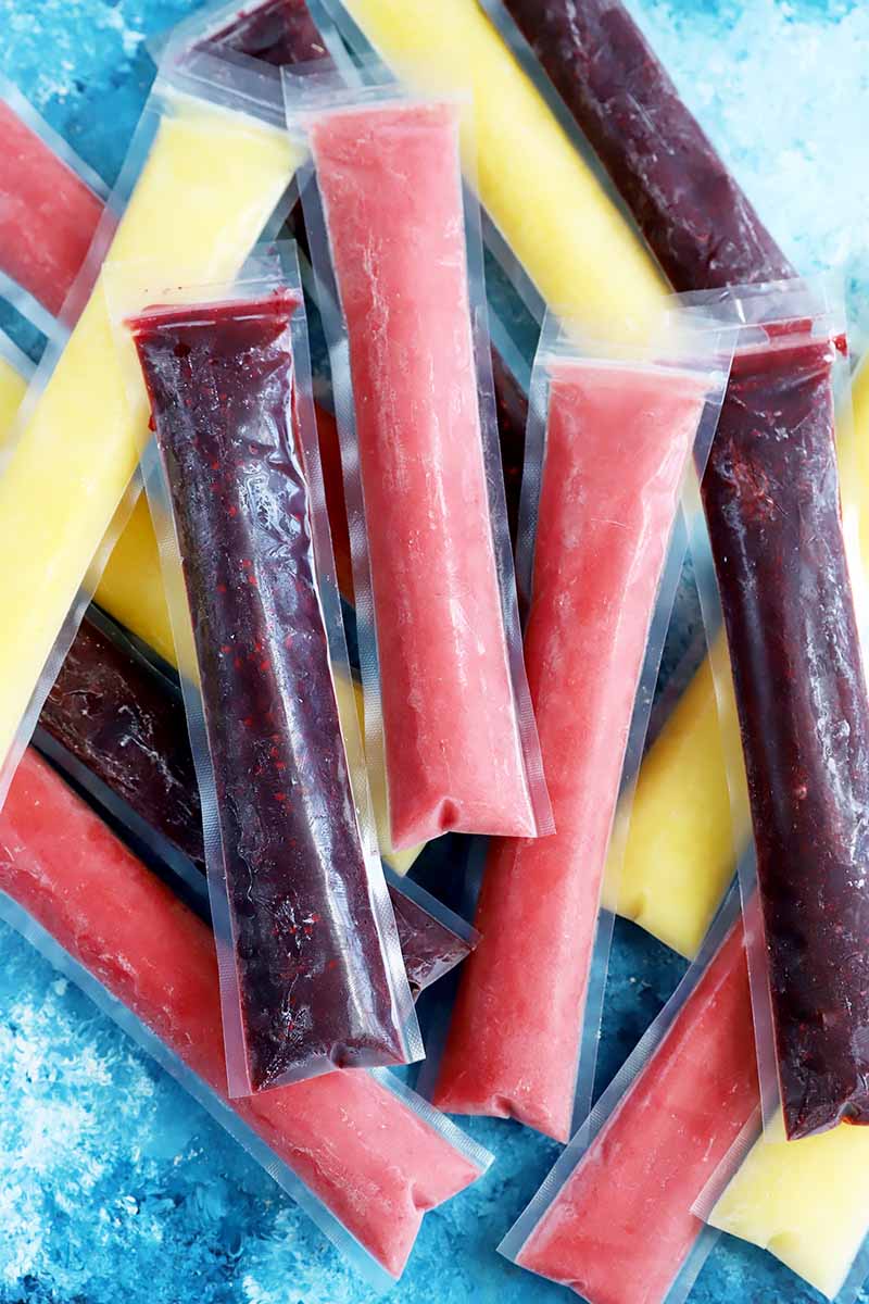 Vertical image of a mound of assorted flavored ice pops.