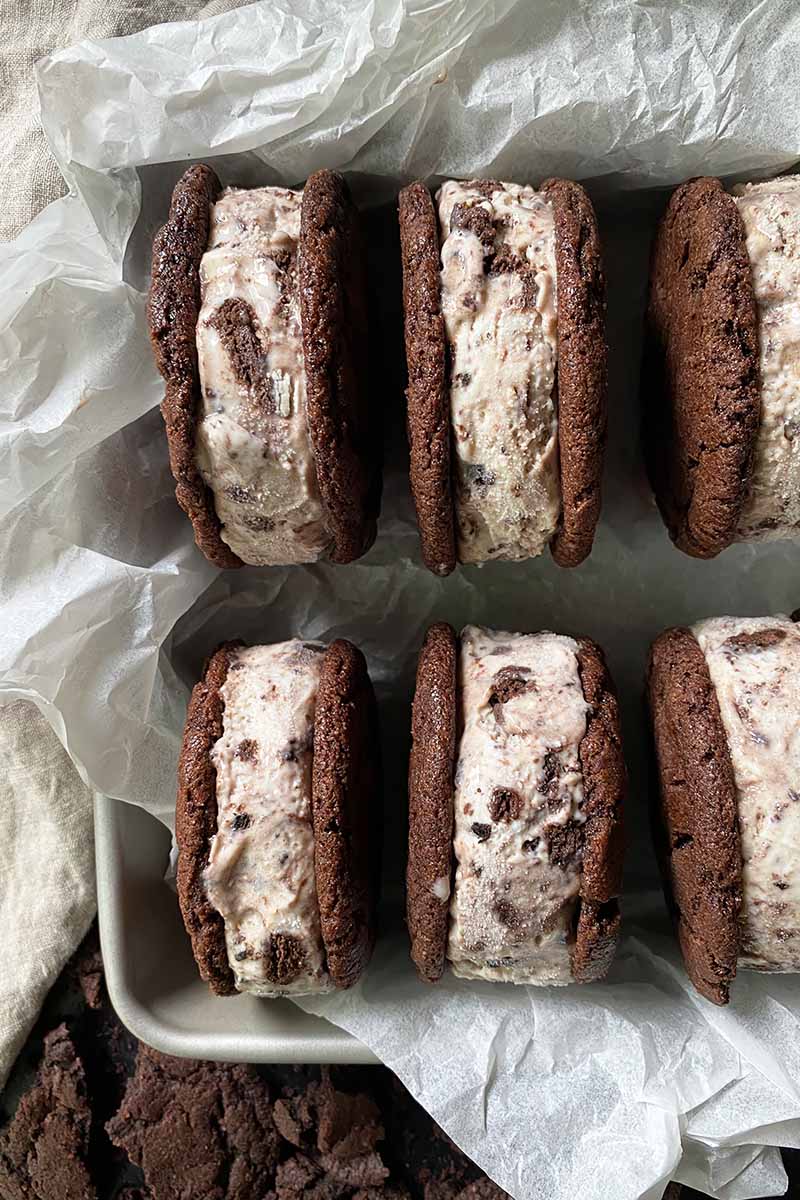 Vertical image of two rows of ice cream sandwiches in a pan lined with crinkled parchment paper.