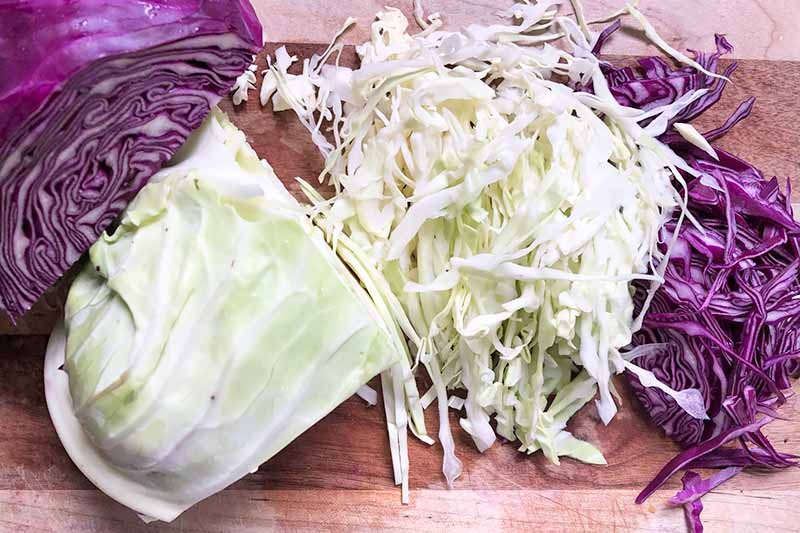 Horizontal image of thinly sliced green and red cabbage on a wooden cutting board.