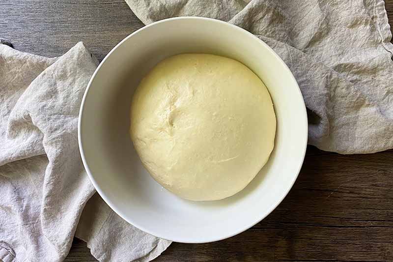 Horizontal image of a risen mound of dough in a large white bowl.
