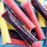 Horizontal image of a mound of assorted flavored frozen treats in long, plastic pouches.