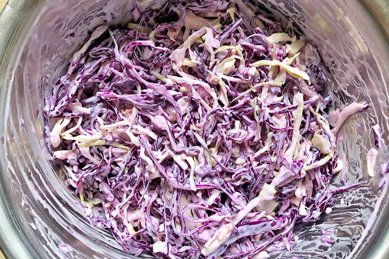 Horizontal image of a creamy mixture with thinly sliced red and green cabbage in a metal bowl.