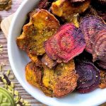 Horizontal close-up image of a white bowl filled with brightly colored and baked thinly sliced beets and parsnips.