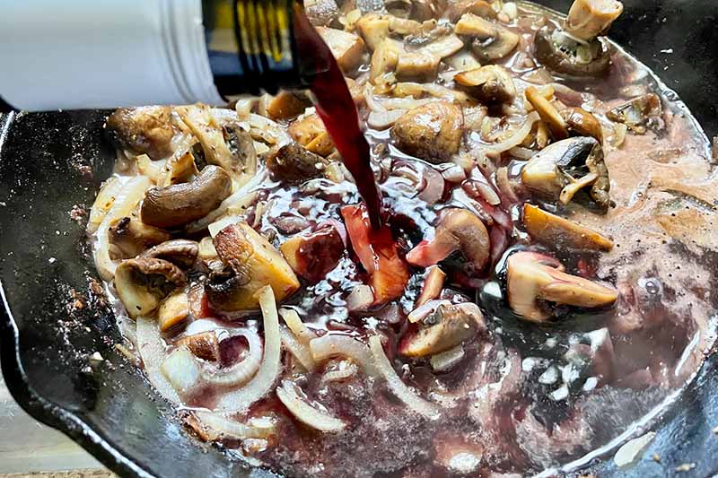 Horizontal image of pouring wine into a sizzling mix of mushrooms in a skillet.