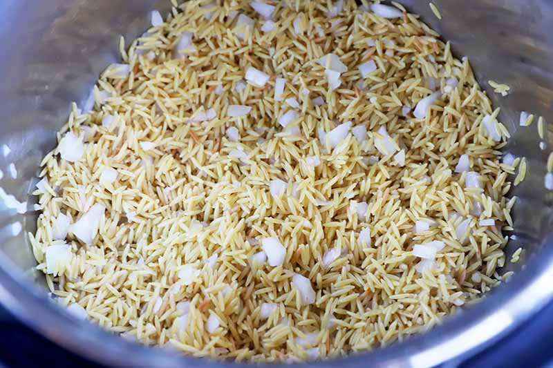 Horizontal image of pasta and chopped onions toasting in a pot.