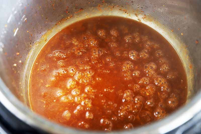 Horizontal image of a bubbling brown sauce in a pot.