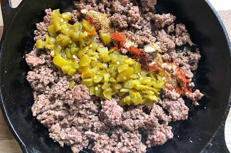 Horizontal image of cooked ground beef topped with salsa in a skillet.