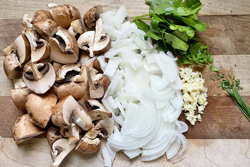 Horizontal image of quartered mushrooms, diced onions, garlic, and herbs.