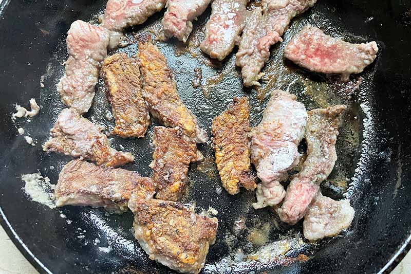 Horizontal image of searing slices of meat in a skillet.