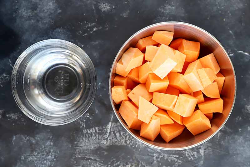 Horizontal image of a bowl of water and a bowl of cubed orange sweet potatoes.