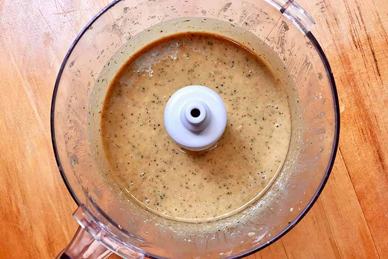 Horizontal image of an herbed tan condiment in a food processor.