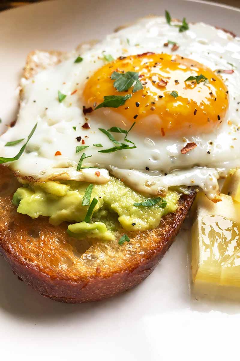 Vertical image of a sunny-side up egg on top of mashed avocado and toast.