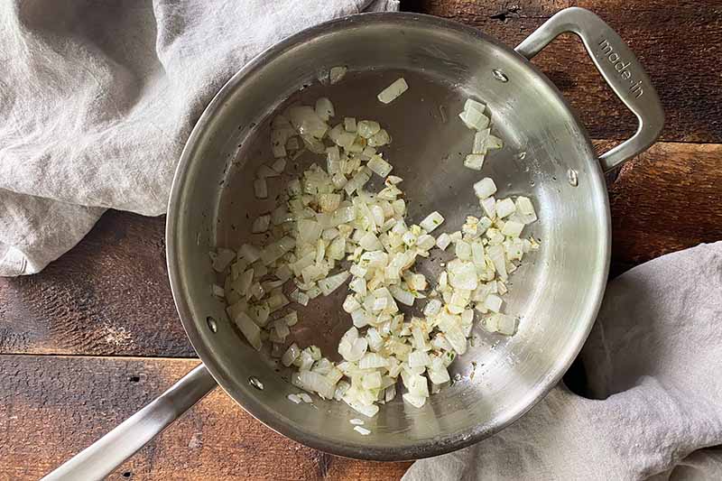 Horizontal image of cooking diced onions in oil in a pot.